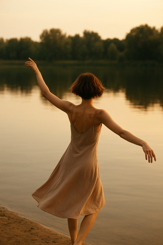 A figure with short brown hair dances gracefully beside a calm lake, immersed in the natural flow and serenity of the water. Face is not visible.