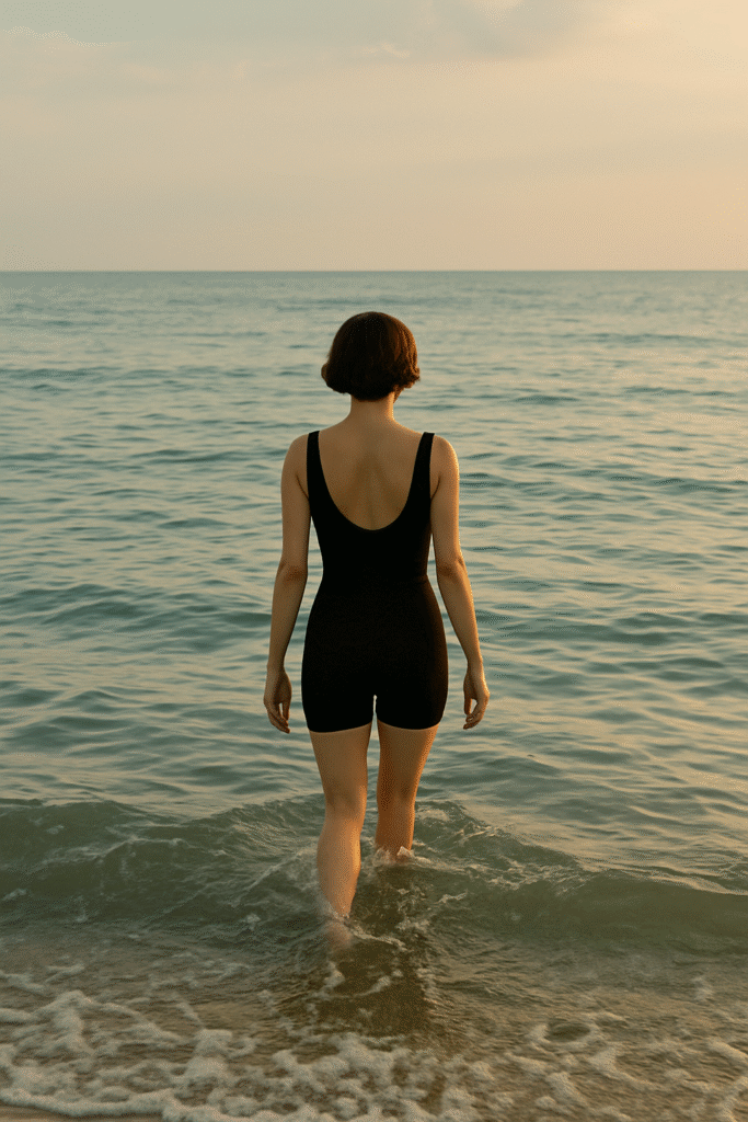 A woman with short brown hair walks into the sea, waves touching her legs, symbolizing calmness, renewal, and healing.